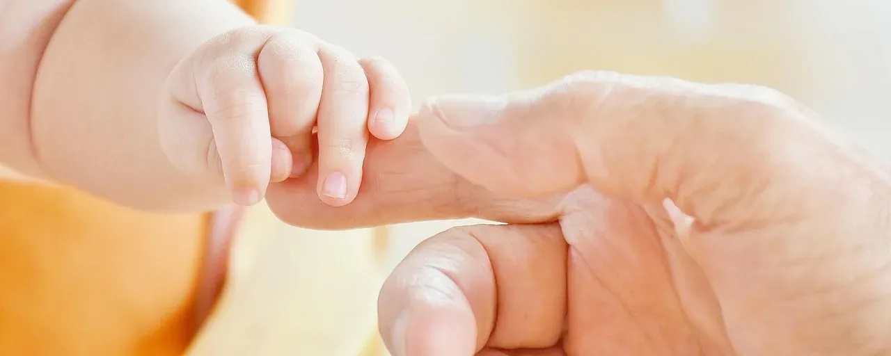 En liten babyhand håller om en vuxens finger