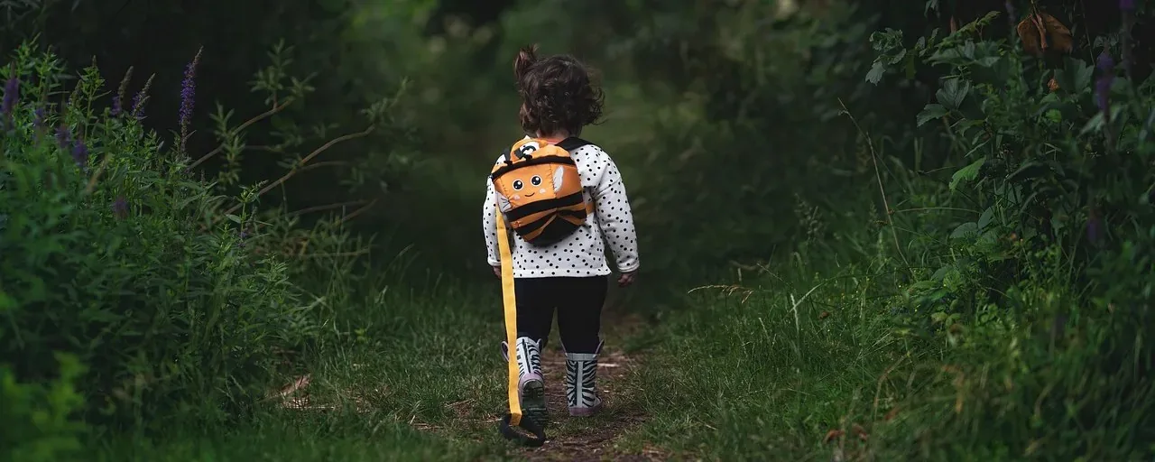 Barn med ryggsäck och stövlar promenerar på en grön stig, sett bakifrån